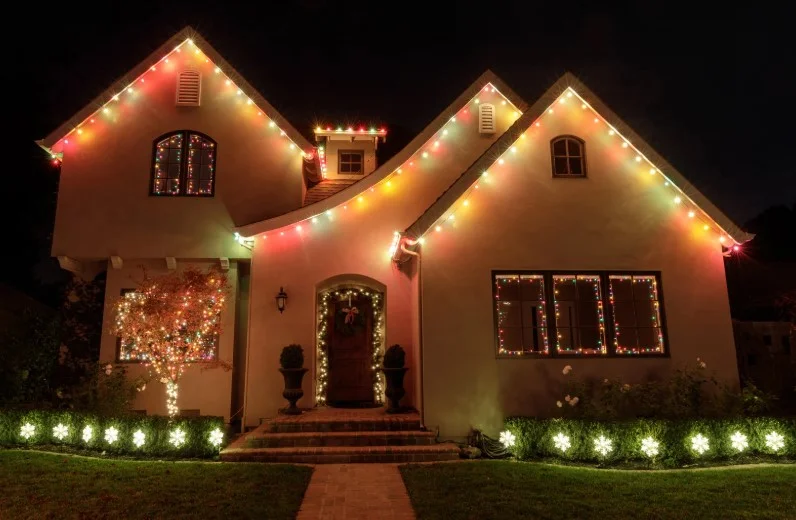 Walkway and roofline holiday lighting with a lit entryway wreath